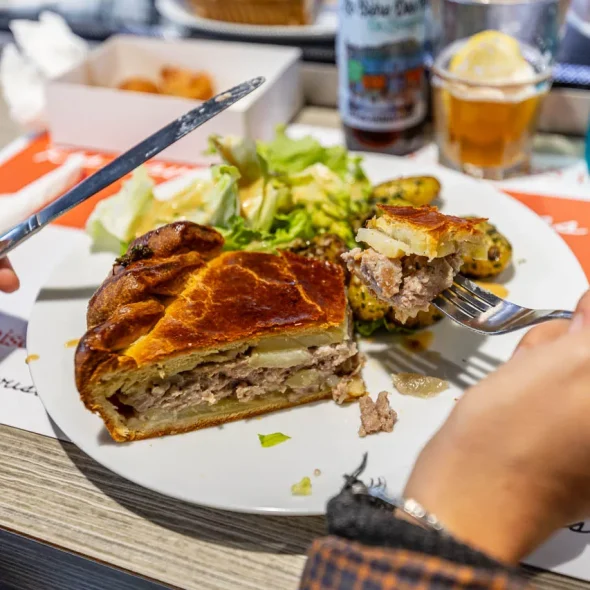 Produits régionaux du Limousin. Personne dégustant un pâté de pommes de terre, une tourte salée à base de pommes de terre et de viande.